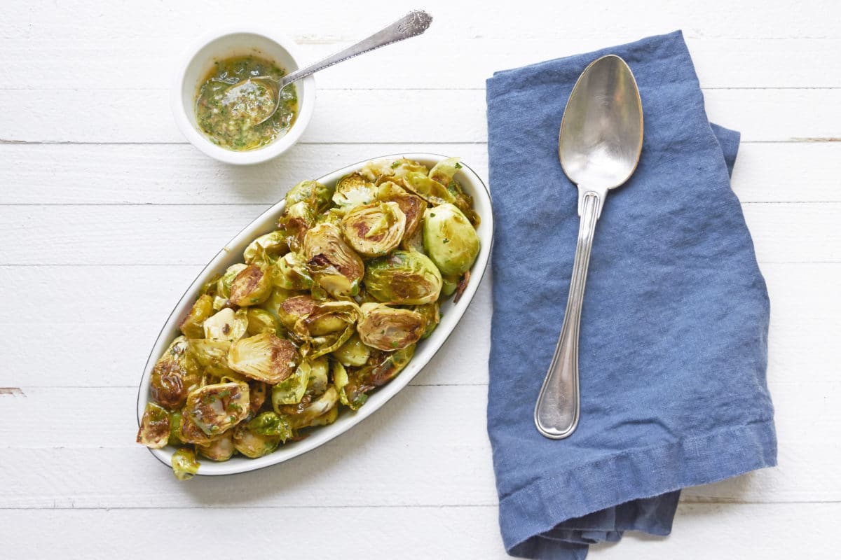 Warm Brussels Sprouts Salad with Anchovy Vinaigrette on platter with napkin and spoon.