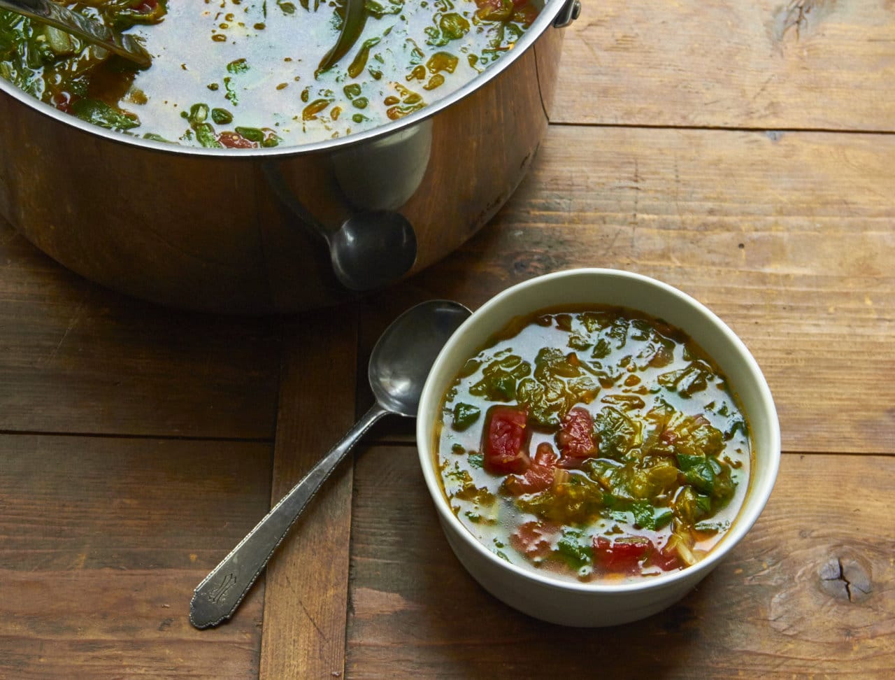 Escarole and Spinach Soup in a bowl near a larger pot of the soup on a wooden surface.