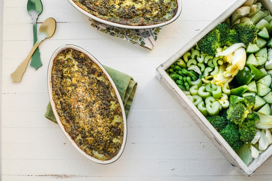 Container of vegetables near bowls of Hot, Creamy Spinach and Goat Cheese Dip.