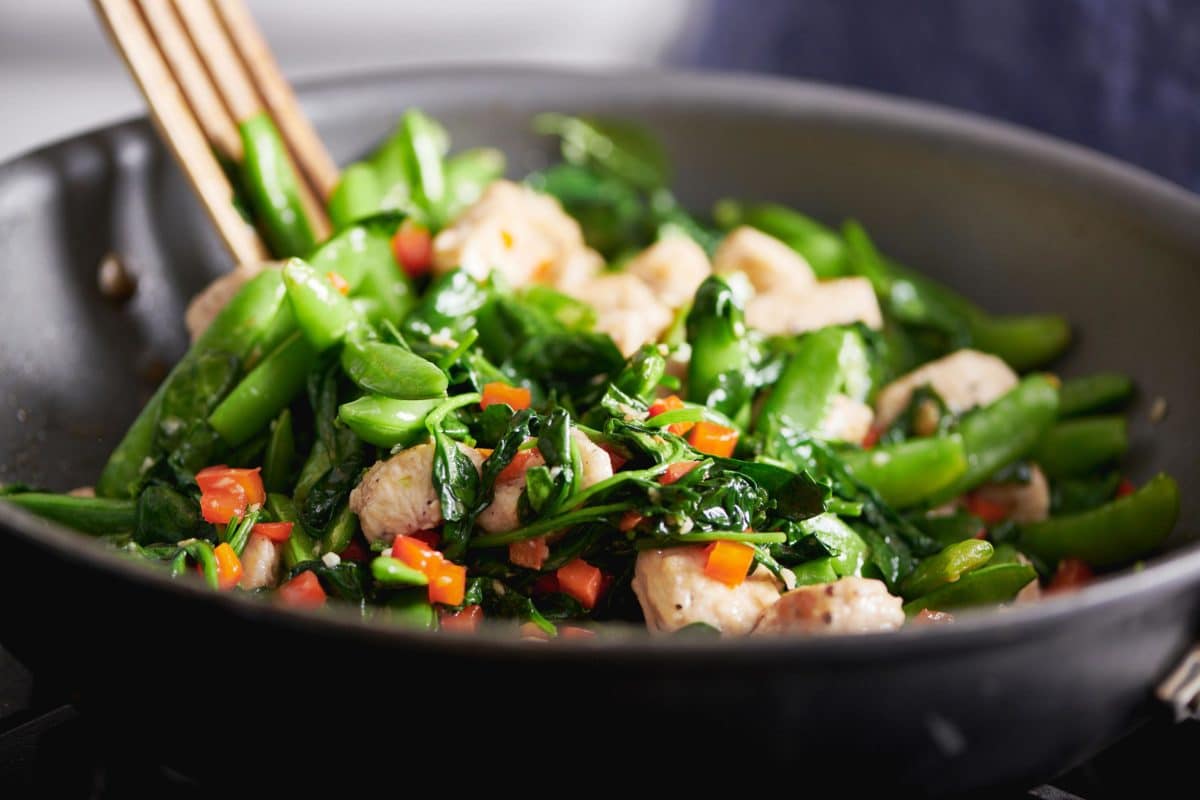 Wooden spatula stirring a pan of Chicken and Spinach Stir-Fry with Ginger and Oyster Sauce.