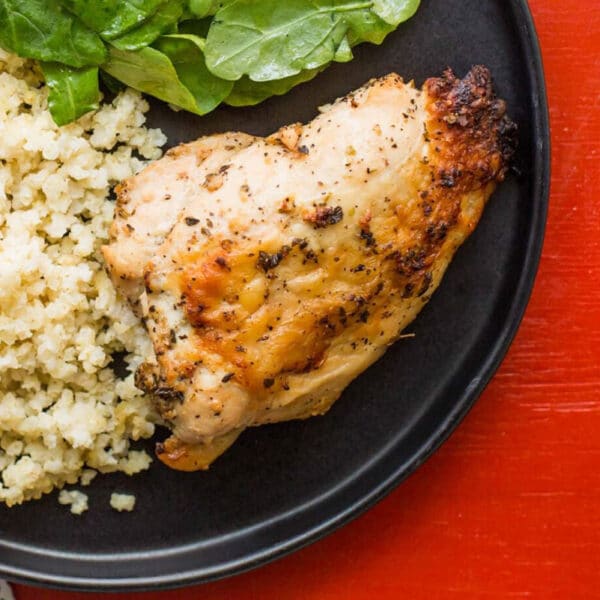 Greek flavored roasted chicken breast on plate with salad and couscous.