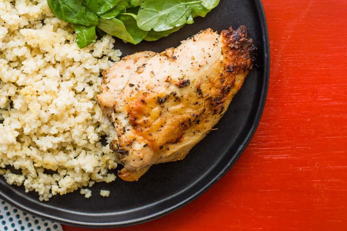 Greek flavored roasted chicken breast on plate with salad and couscous.