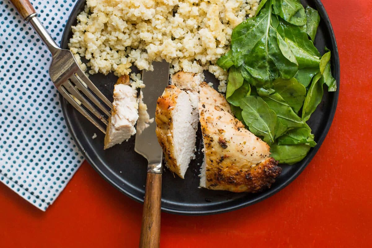 Greek Roasted Chicken Breasts on plate with rice and salad.