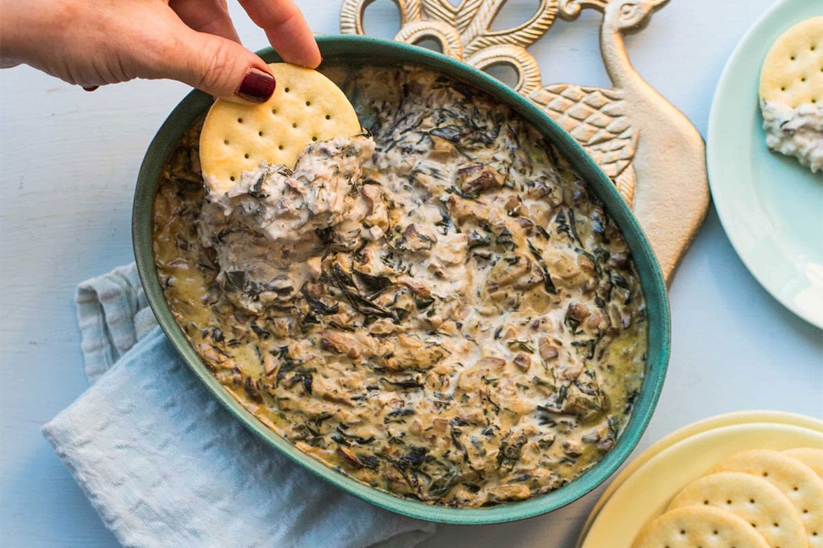 Woman dipping a cracker into baked mushroom spinach dip.
