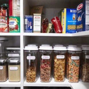 Clear, labeled containers of food on white shelves.