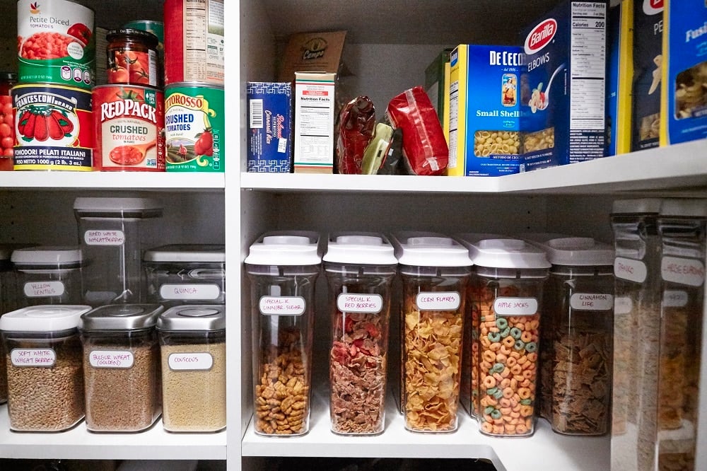 Clear, labeled containers of food on white shelves.