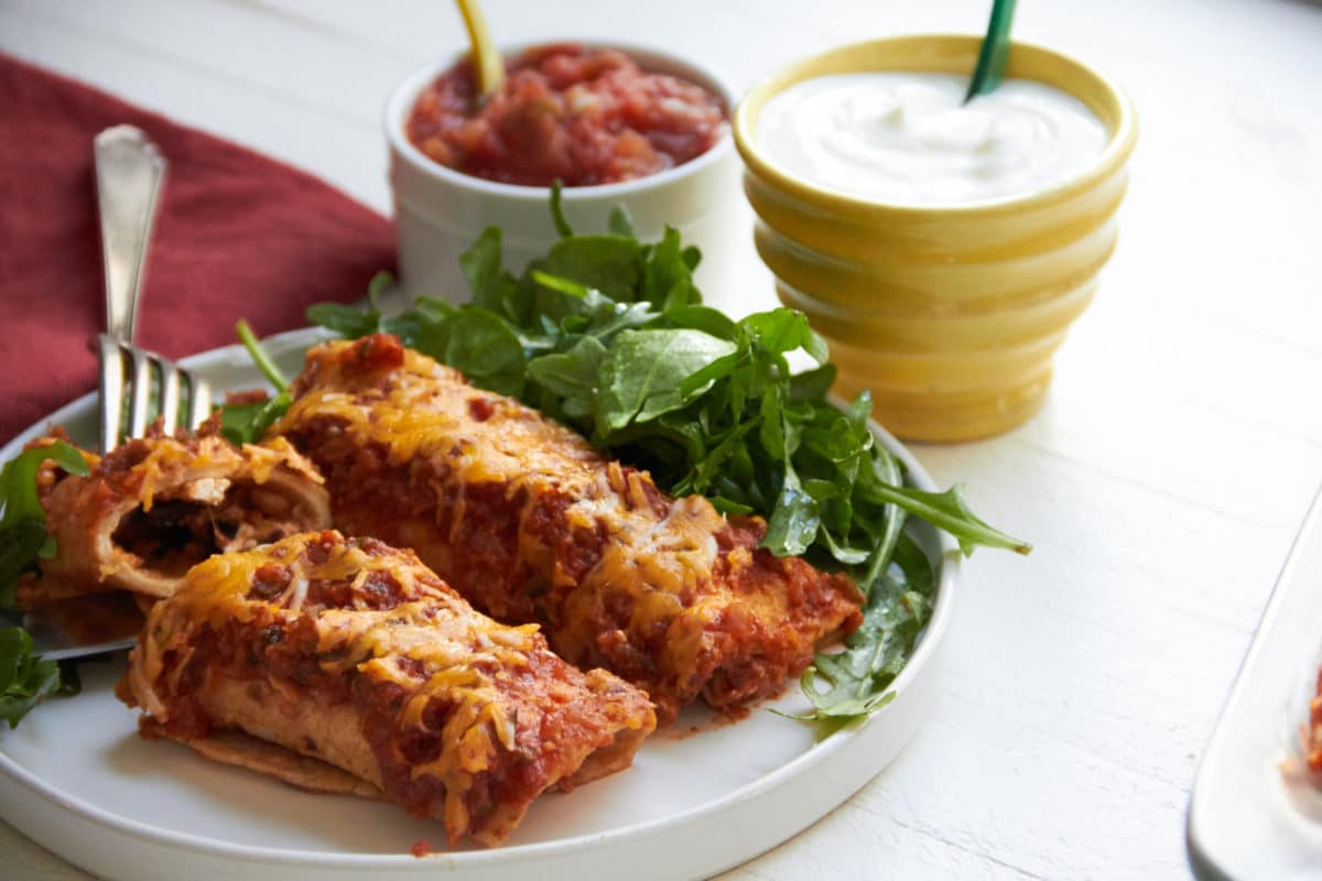 Spicy Chicken and Black Bean Enchiladas on white plate.
