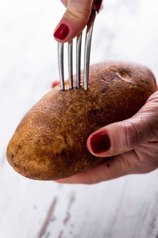 Woman using a fork to poke holes into a potato.