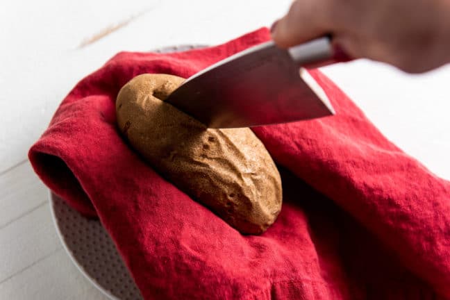 Large knife slicing into a baked potato.