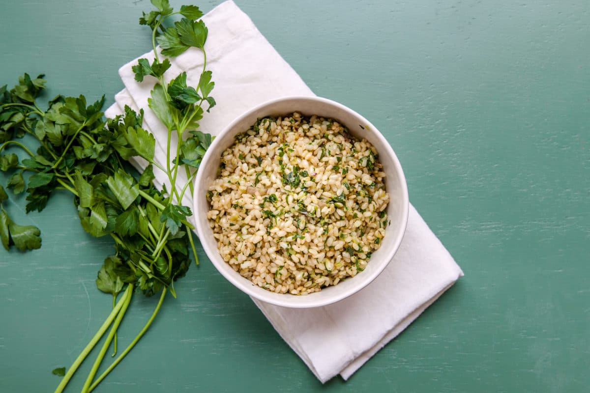 Herby Brown Rice in bowl next to fresh sprigs of parsley.