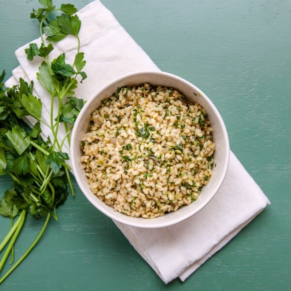 Herby Brown Rice in bowl next to fresh sprigs of parsley.