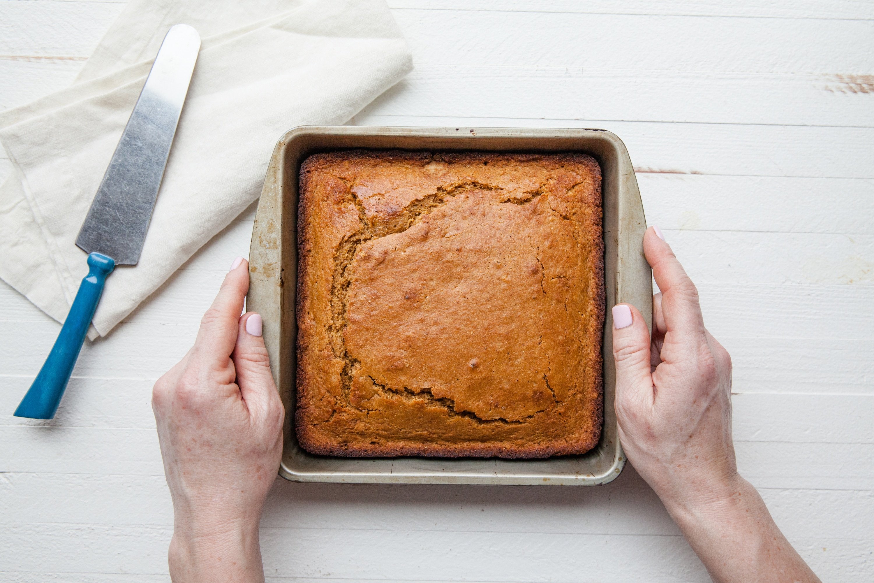 Woman putting down pan of Molasses Cornbread on a white surface.