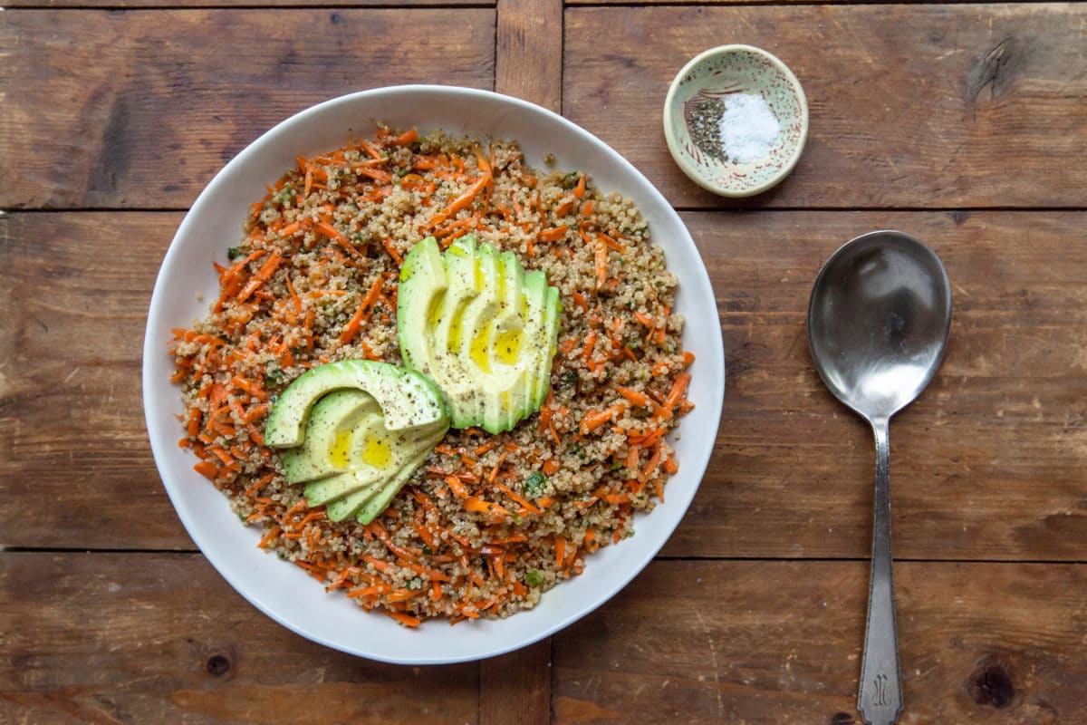 Sesame-Honey Quinoa and Carrot Salad in white bowl, topped with Sliced Avocado.