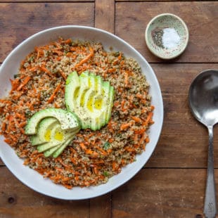 Sesame-Honey Quinoa and Carrot Salad in white bowl, topped with Sliced Avocado.