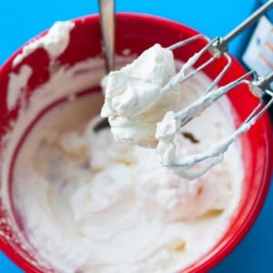 Fresh whipped cream in red bowl with mixer.