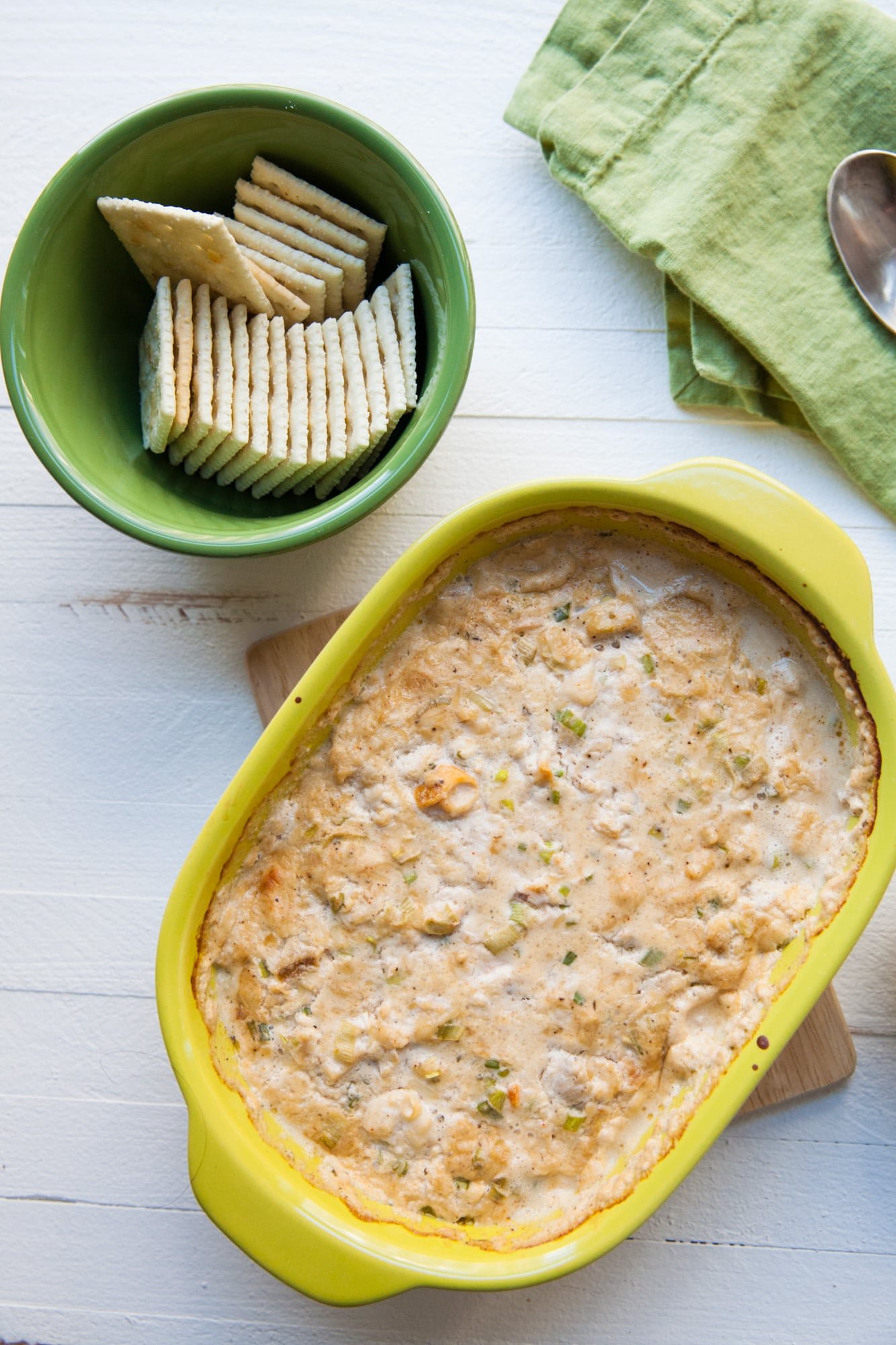 Hot Cheesy Clam Dip in a yellow serving dish with crackers nearby.