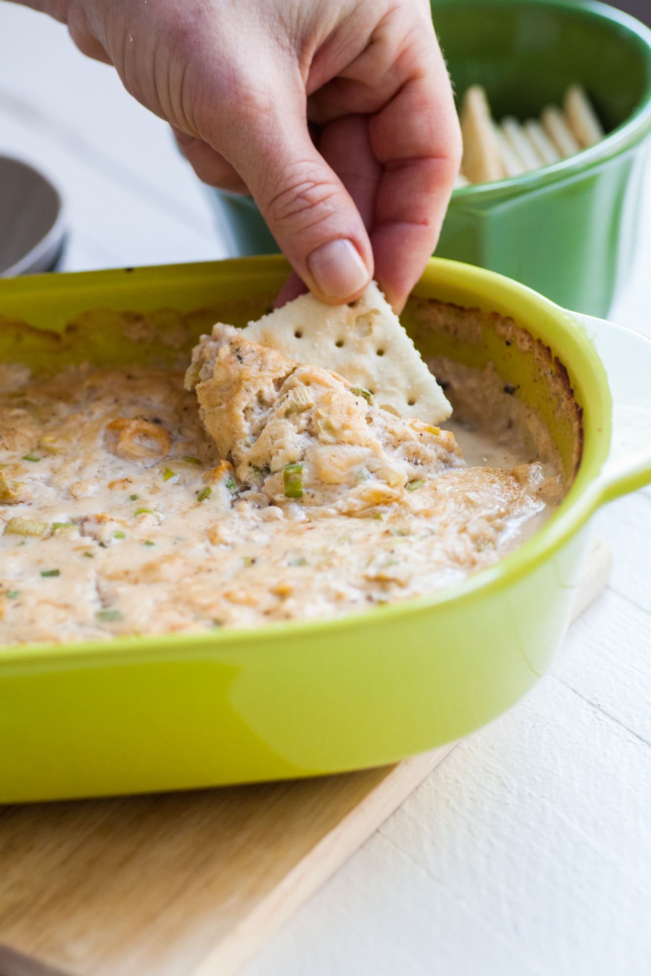 Woman dipping saltine into a serving dish of hot clam dip.
