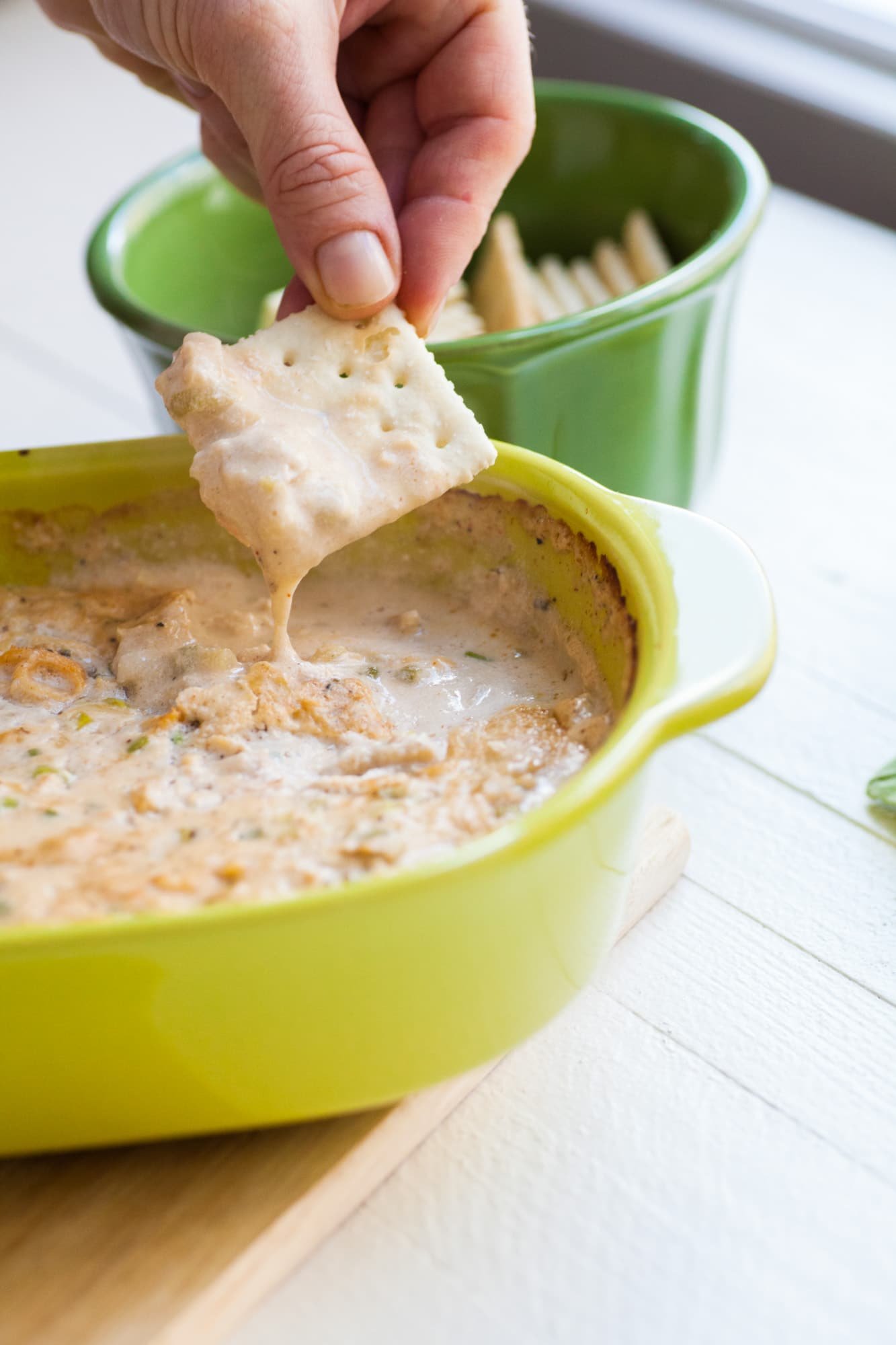 Woman dipping into hot clam dip with a cracker.