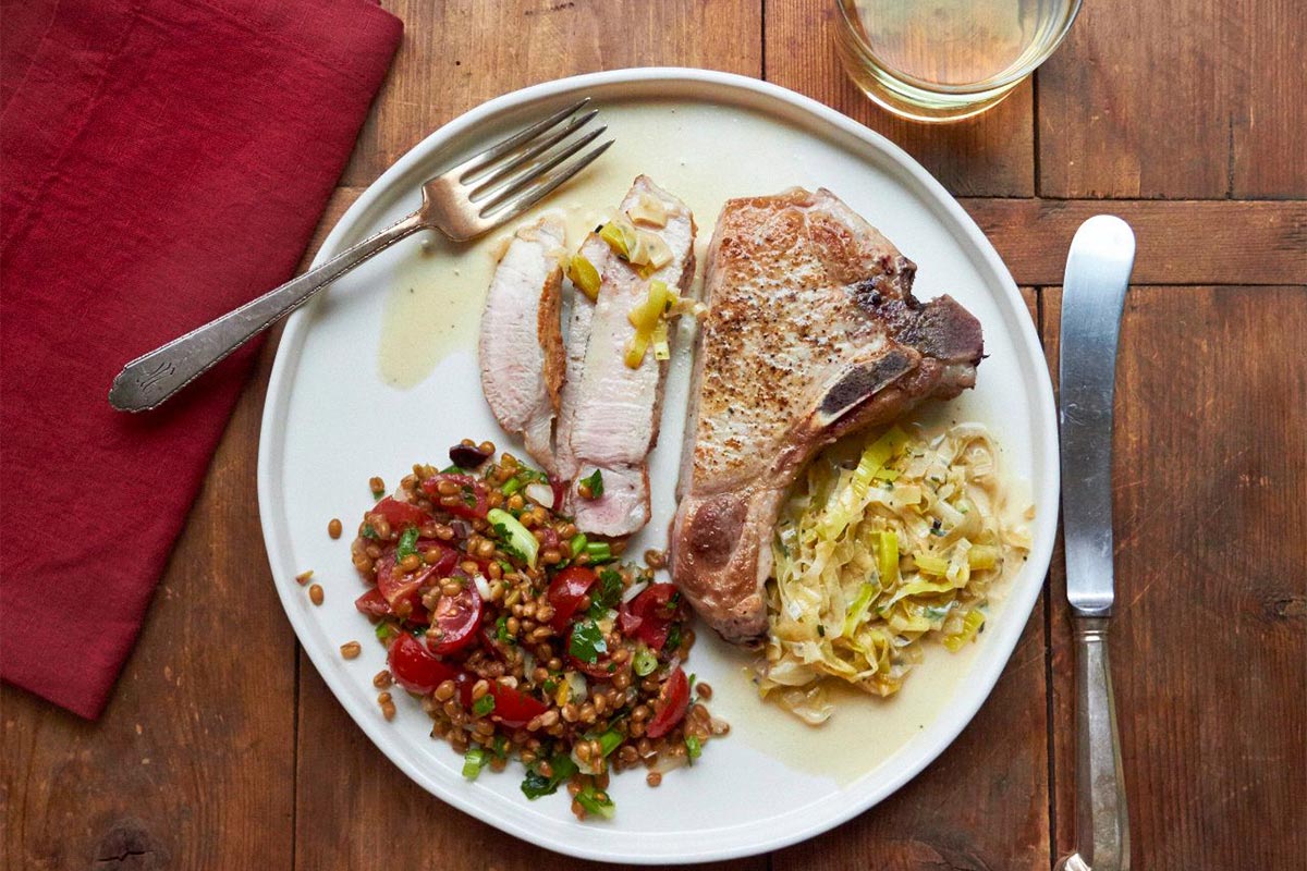 Pork chop on plate with creamy madeira sauce and other sides.