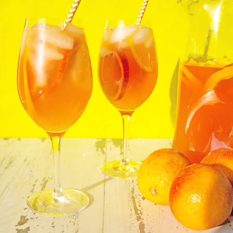 Two long-stemmed glasses of Orange White Wine Campari Sangria.