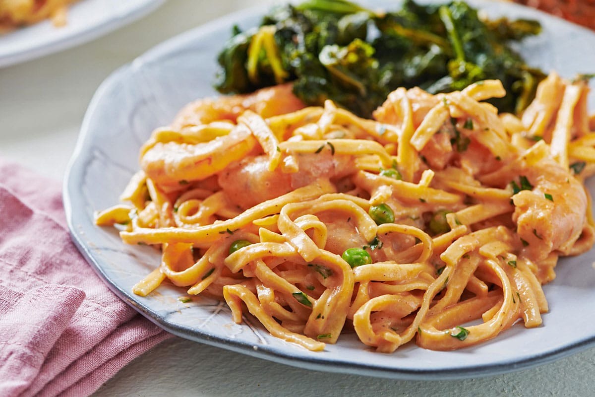 Fresh linguine with shrimp and peas in a pink cream sauce on a plate.