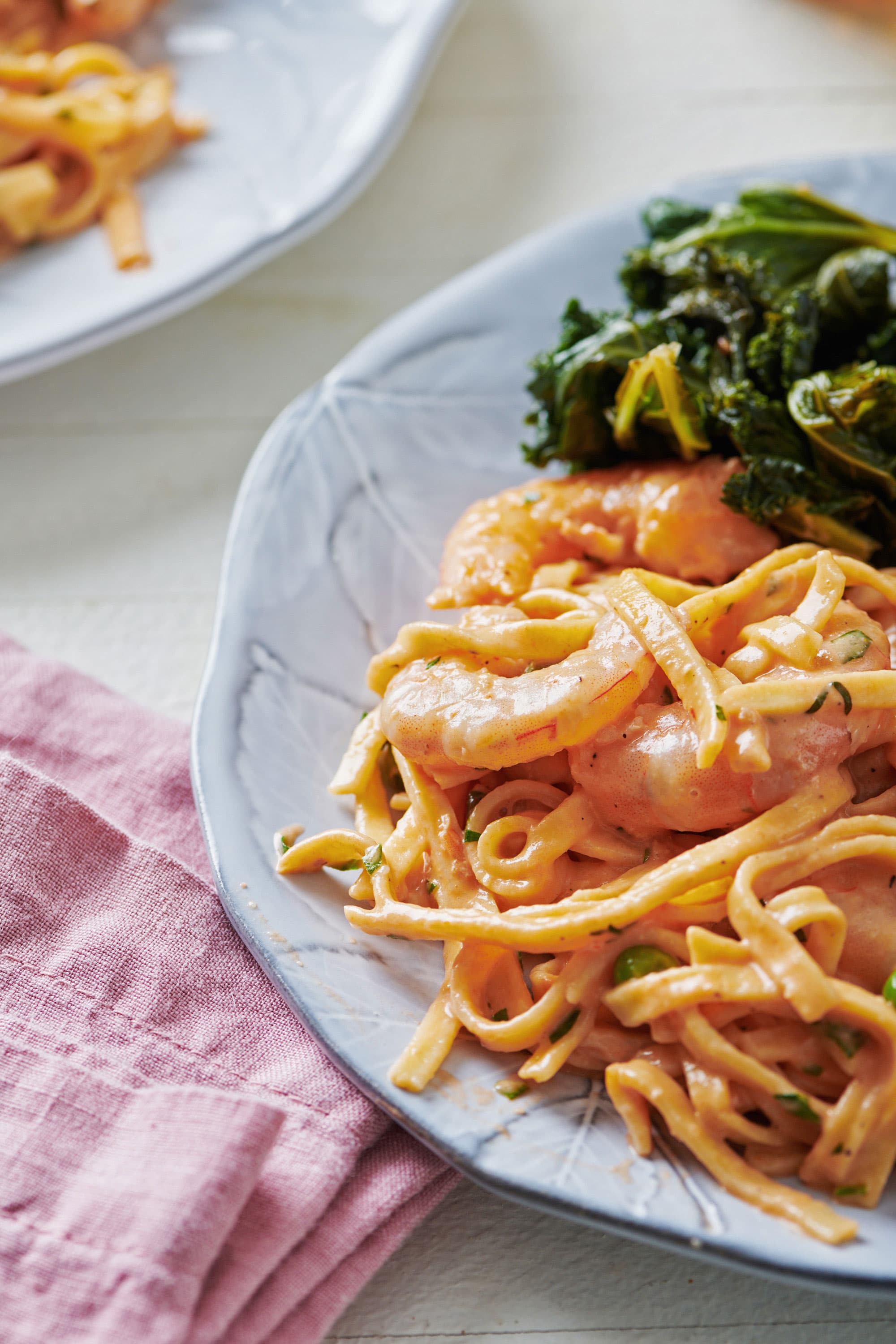 Plate with fresh linguine with shrimp and peas in a pink cream sauce and greens.