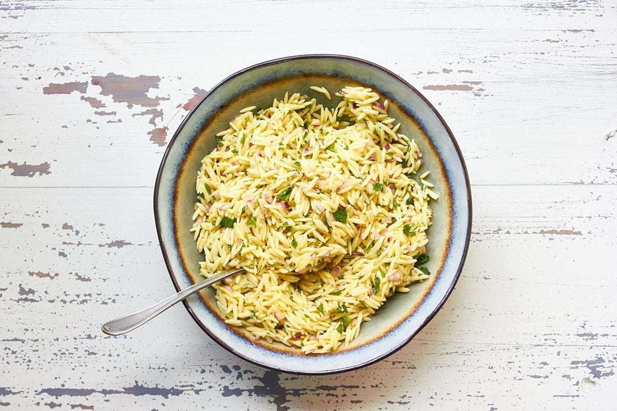 Orzo pasta salad with red onion and mint in serving bowl.