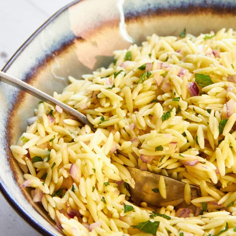 Orzo pasta salad with red onion and mint in serving bowl with spoon.