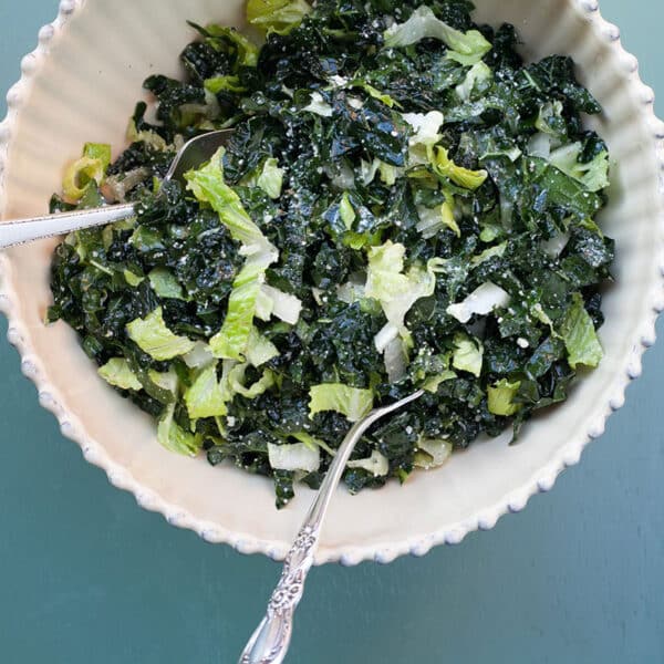 White bowl filled with a salad of romaine lettuce and kale with a lemon dressing.