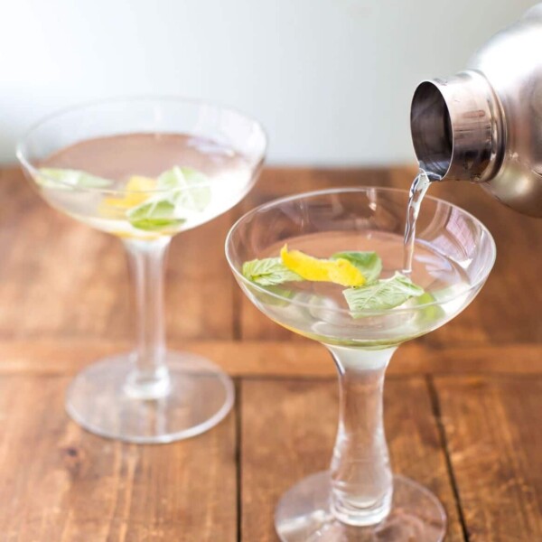 Pouring Basil Ginger Lemon Saketini from cocktail shaker into martini glasses.