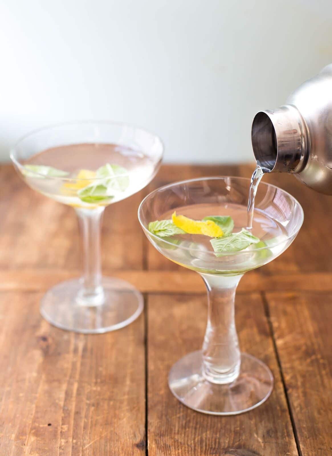 Pouring Basil Ginger Lemon Saketini from cocktail shaker into martini glasses.