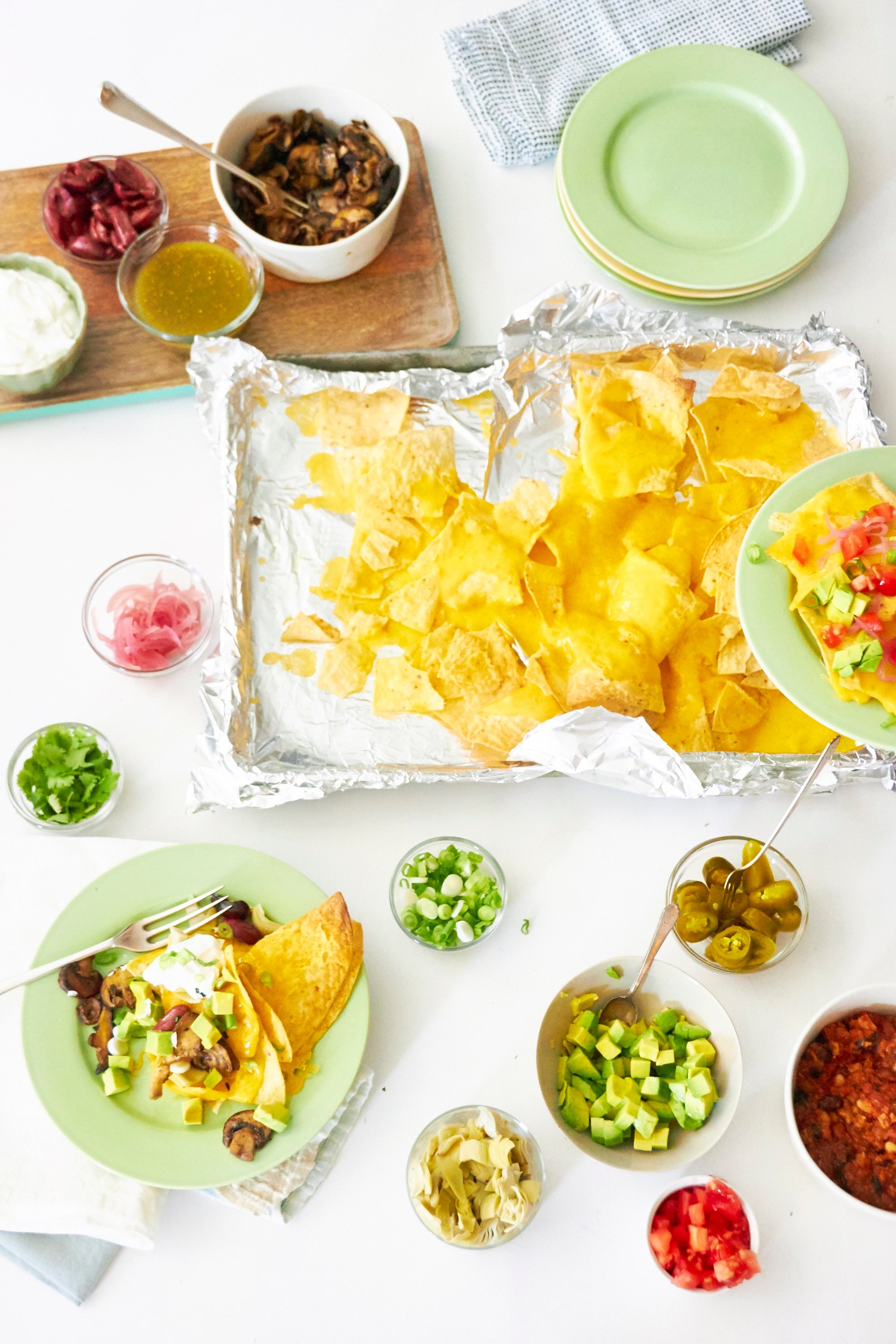 Nachos on a foil covered baking sheet surrounded with various toppings in small bowls