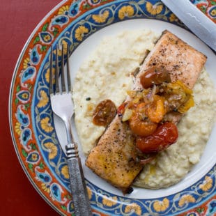 Fork, knife, and Salmon with Polenta and Warm Tomato Vinaigrette on a colorful plate.