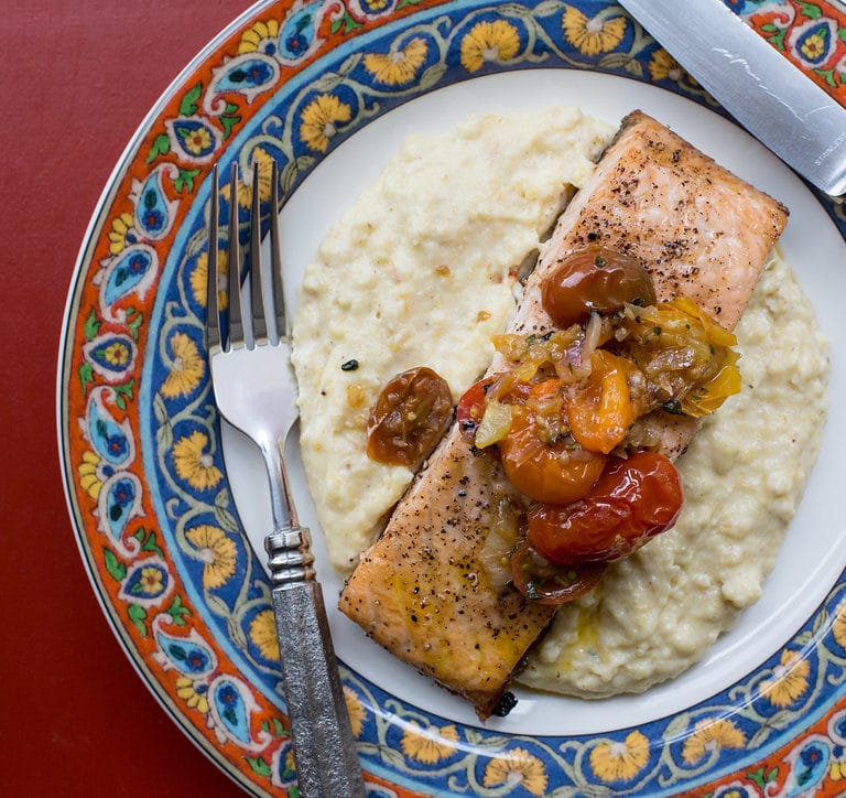 Fork, knife, and Salmon with Polenta and Warm Tomato Vinaigrette on a colorful plate.