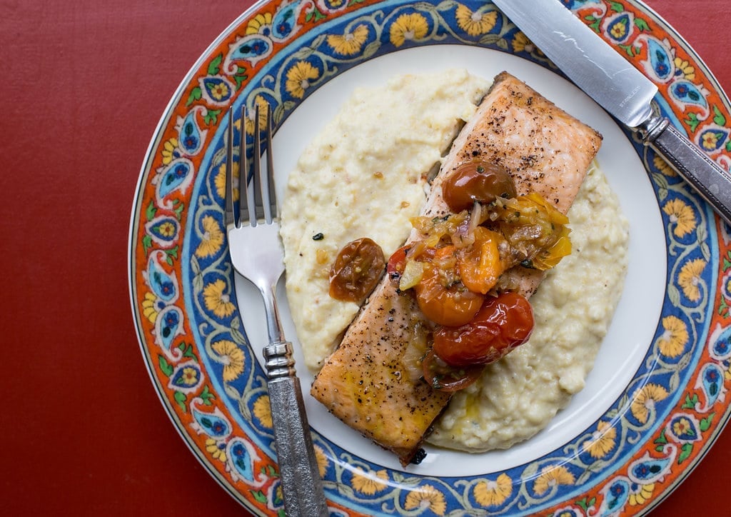 Fork, knife, and Salmon with Polenta and Warm Tomato Vinaigrette on a colorful plate.