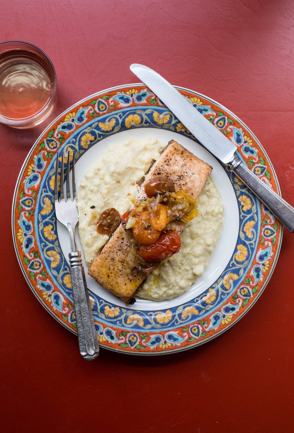 Plate of Salmon with Polenta and Warm Tomato Vinaigrette on a red table.