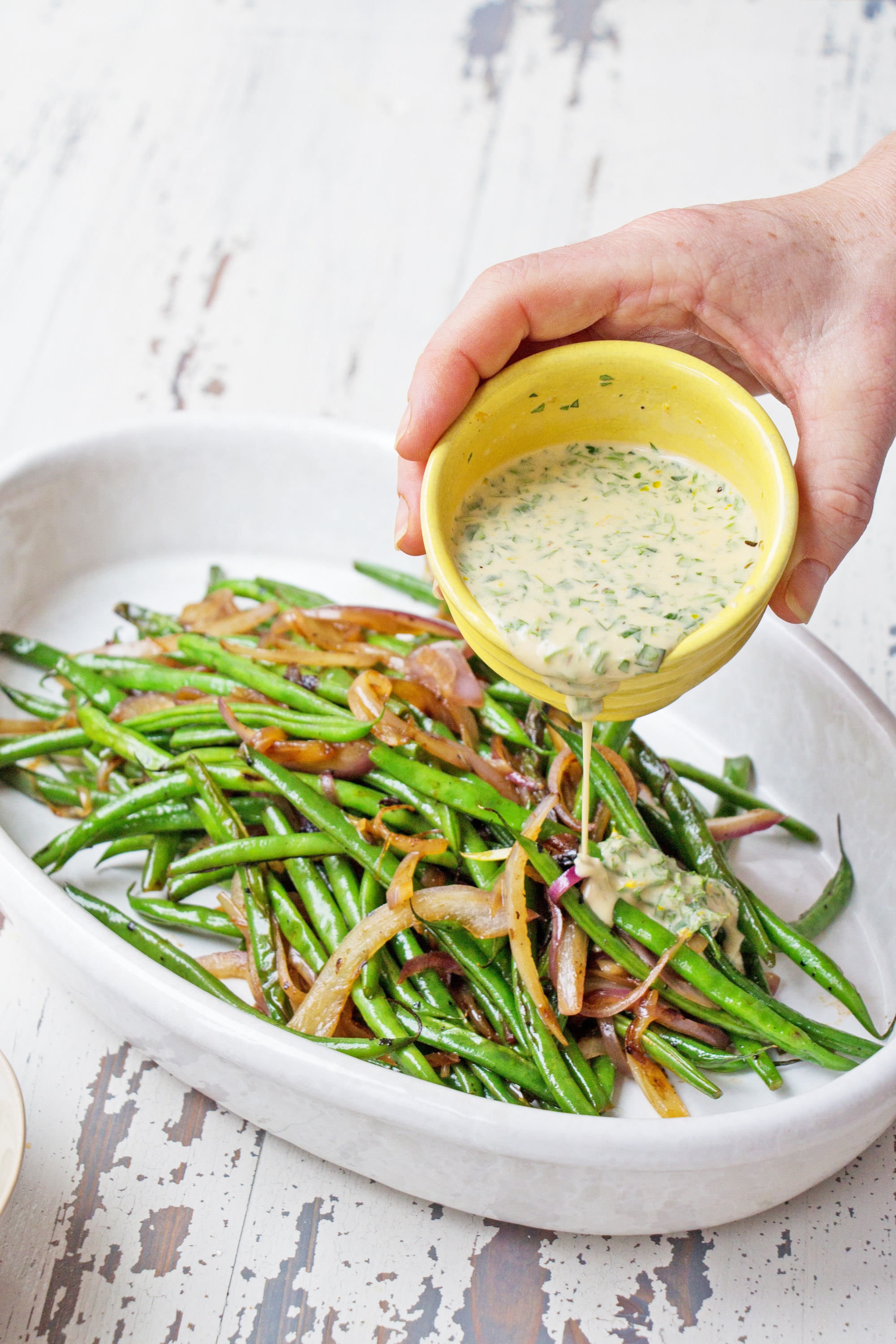 Pouring dressing over haricots verts and red onions.