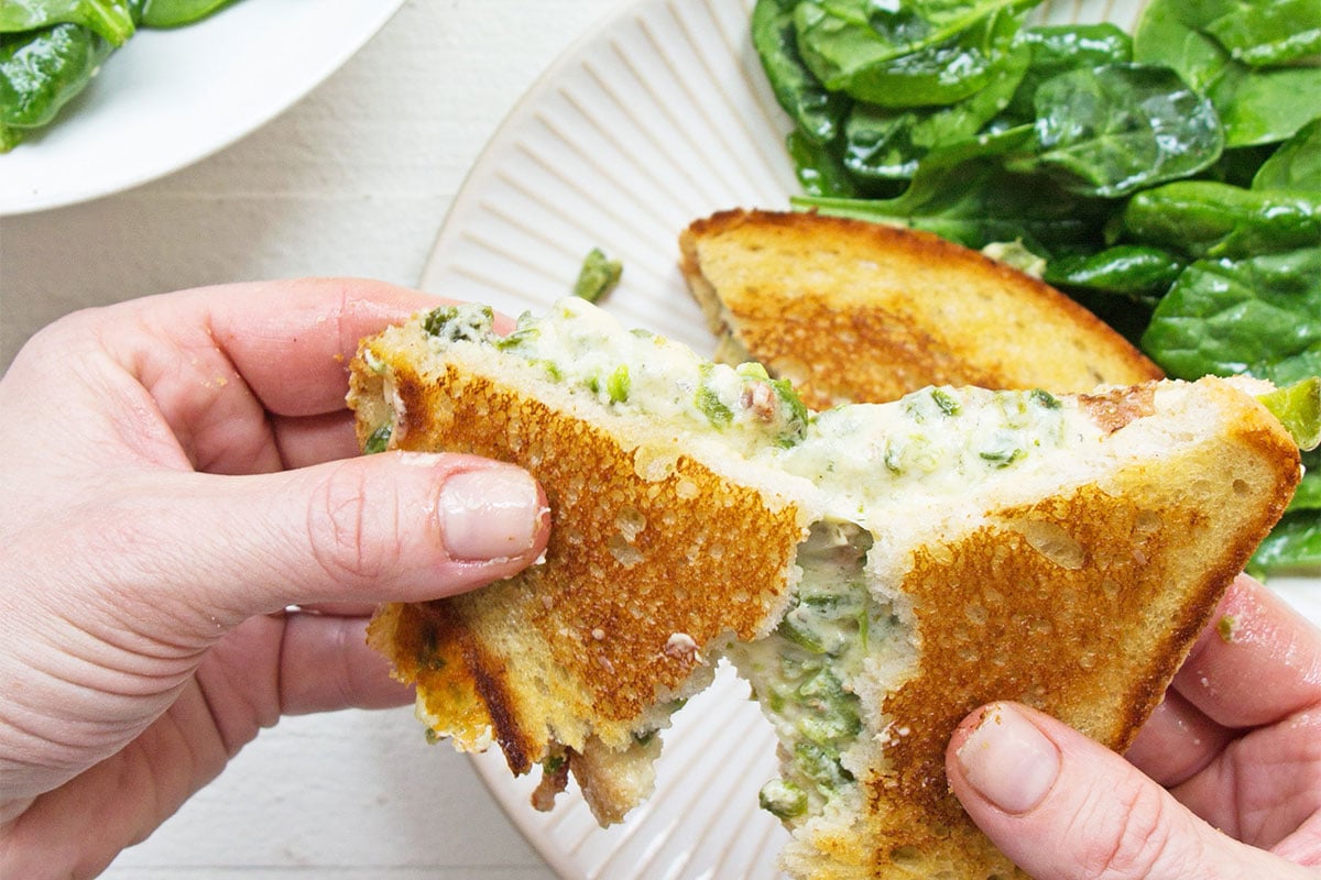 Woman holding a Jalapeno Popper Grilled Cheese sandwich over a plate of salad.