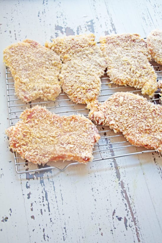 Breaded, raw chicken cutlets on a wire rack.