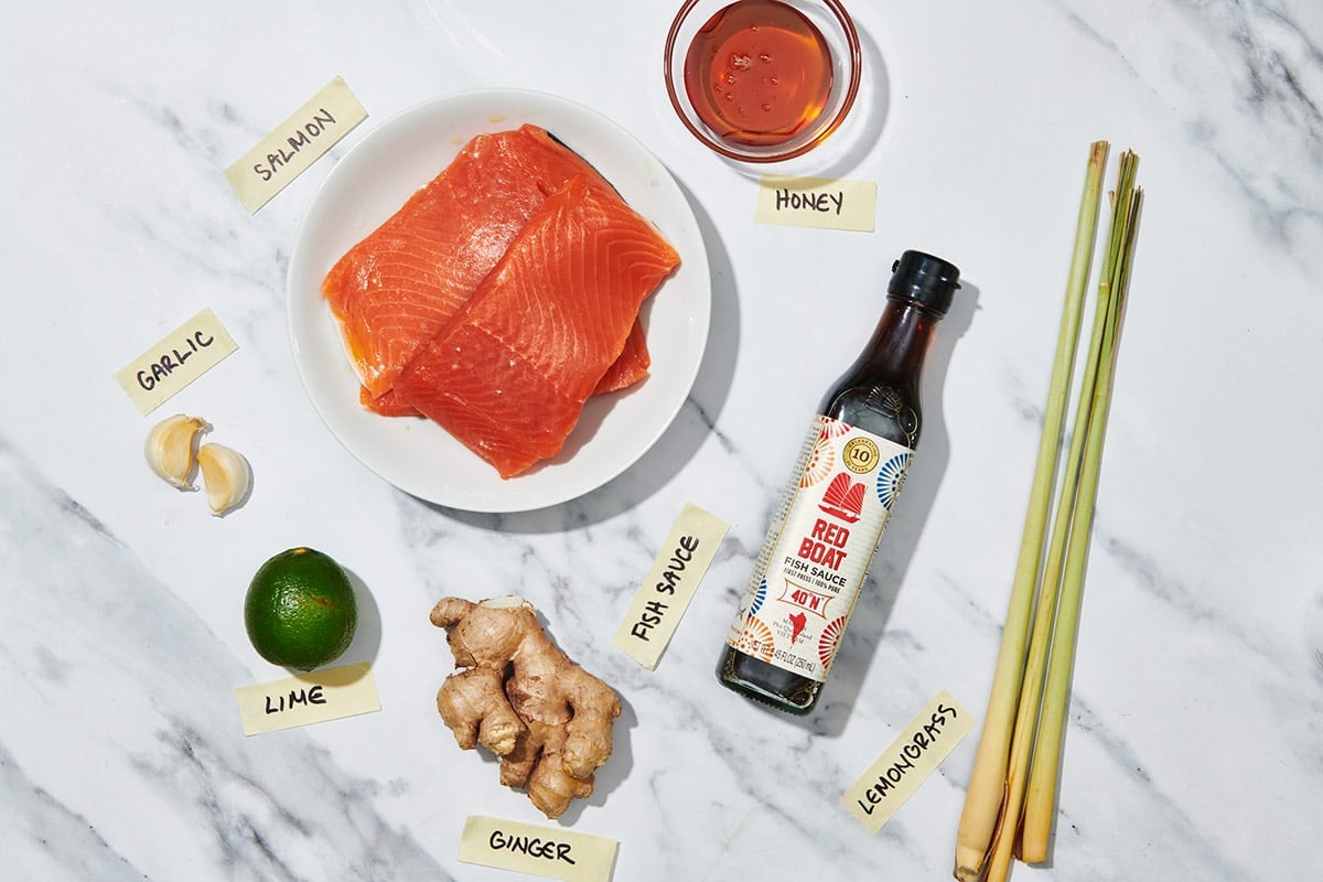 Raw salmon, fresh ginger and lemongrass, and other ingredients on marble table.