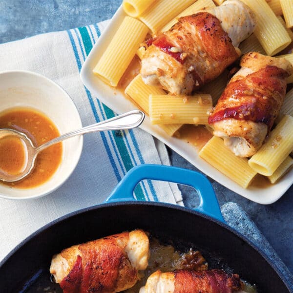 Chicken rolls wrapped in bacon on table with pasta and Marsala sauce.