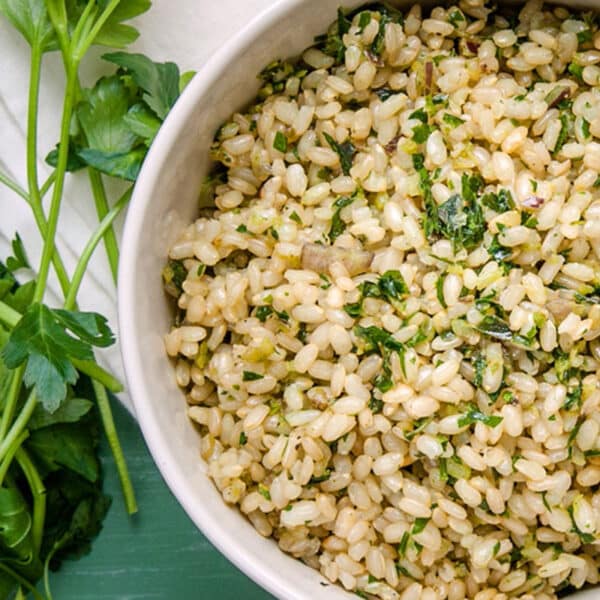 Herb-flavored brown rice in white bowl next to fresh parsley.