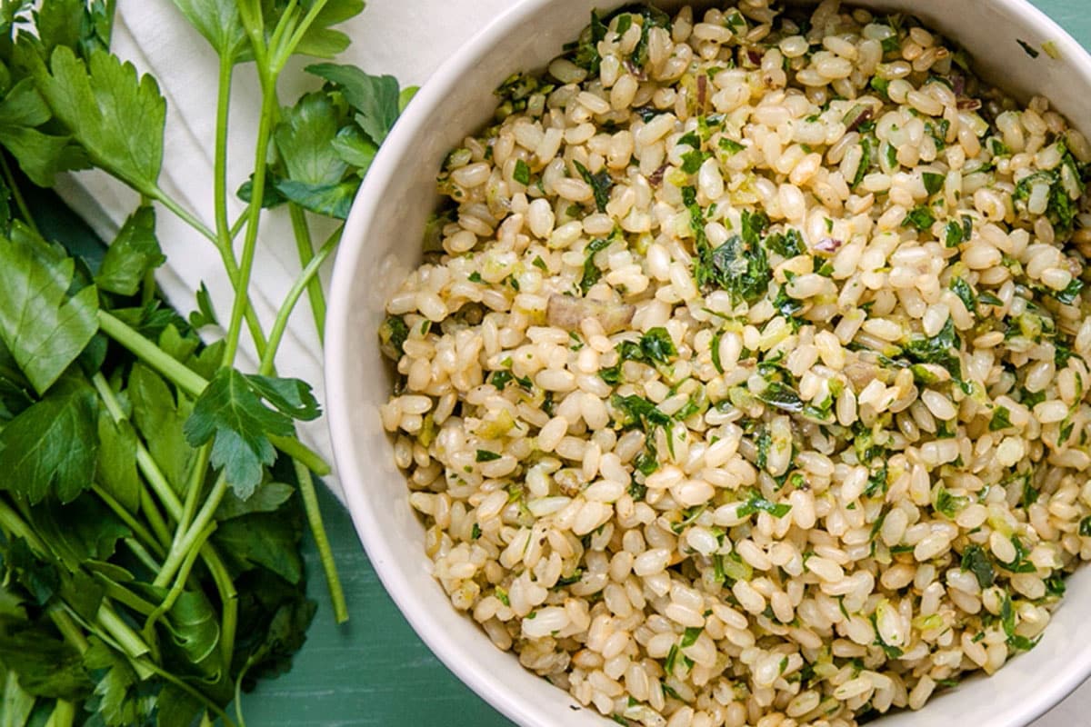 Herb-flavored brown rice in white bowl next to fresh parsley.