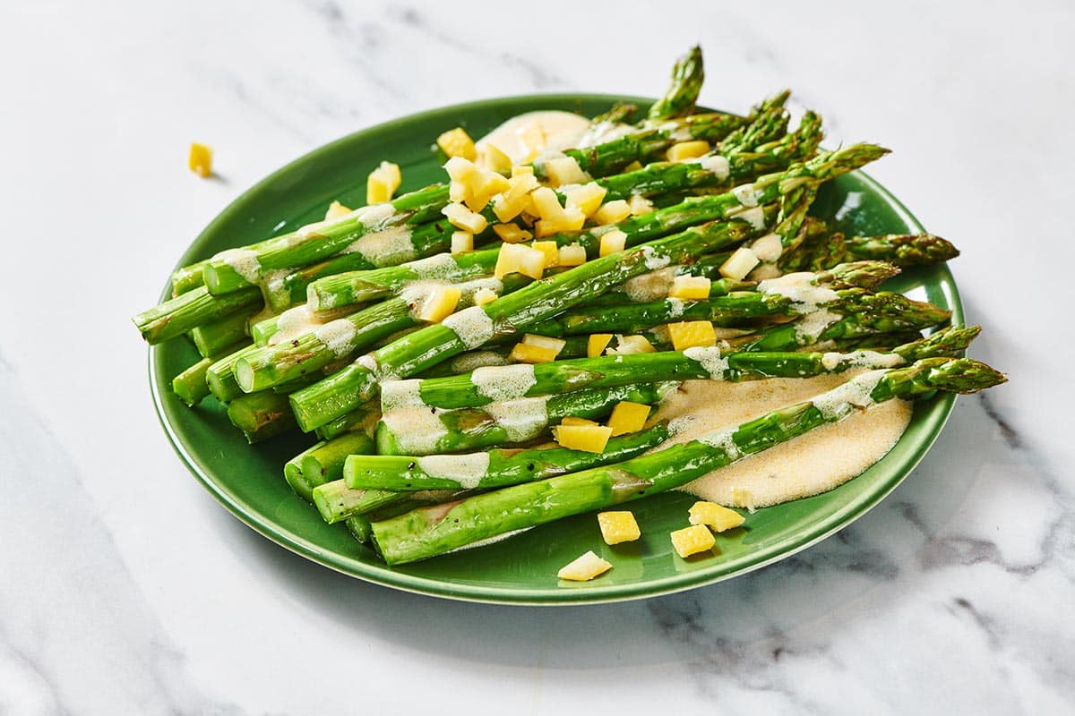 Green plate on table with roasted asparagus topped with lemon dressing.
