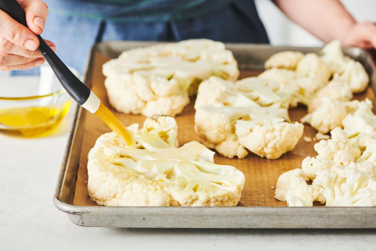 Cauliflower steaks being brushed with oil.