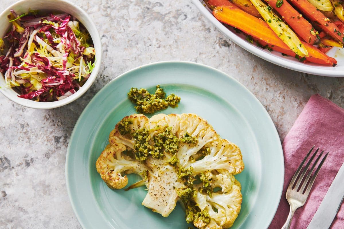 Small blue plate of a Roasted Cauliflower Steak topped with Tapenade.