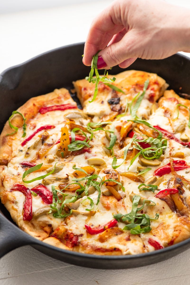 Woman sprinkling basil onto a Fontina and Havarti Cast Iron Pan Pizza.