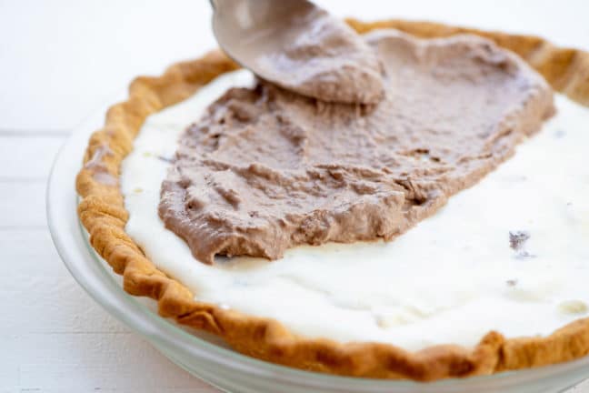 Spoon spreading chocolate ice cream onto a chocolate peanut butter ice cream pie.