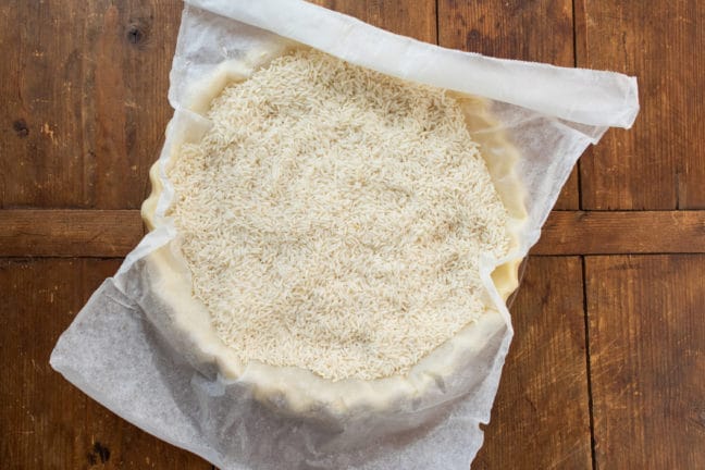 Pie crust topped with parchment paper and filled with rice.