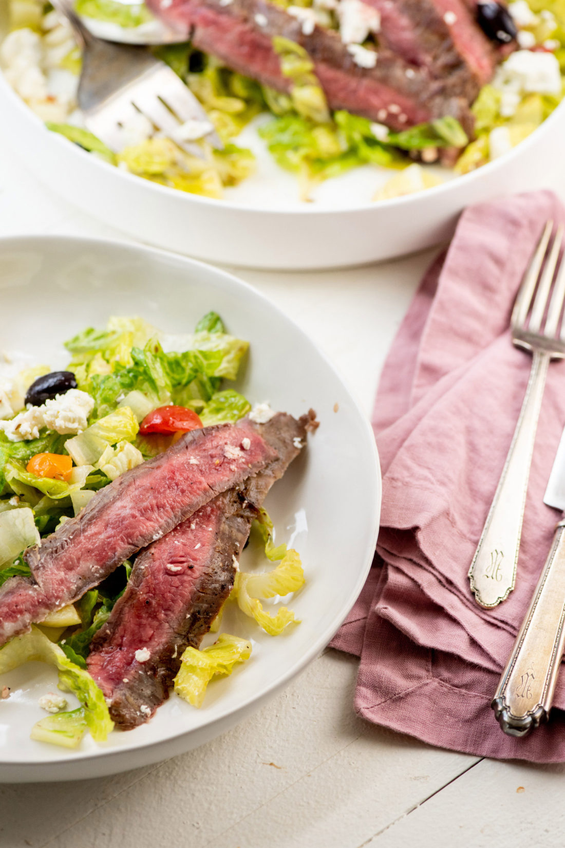 Silverware and cloth napkins next to a plate of Greek Salad with Flank Steak.